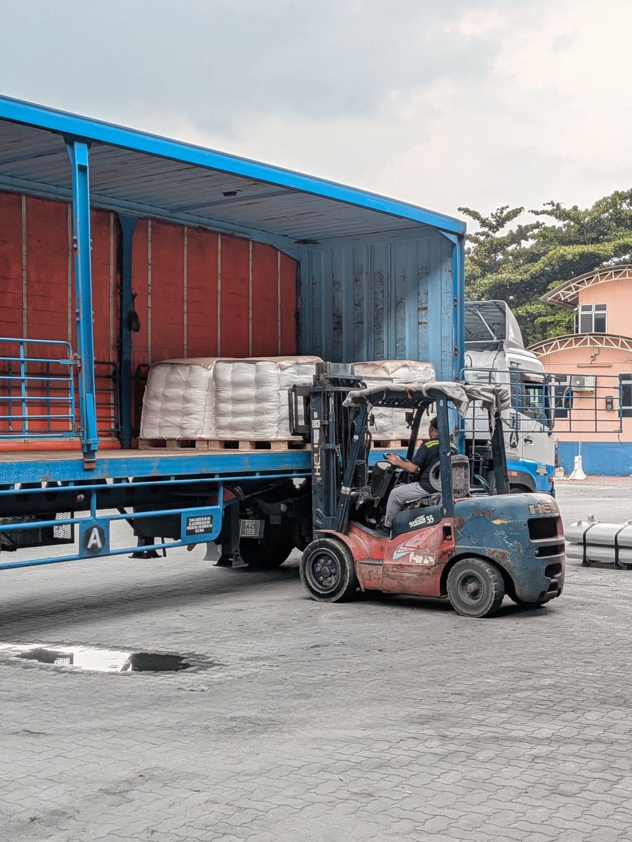 A forklift loading pallets into a curtain-sided truck at a depot