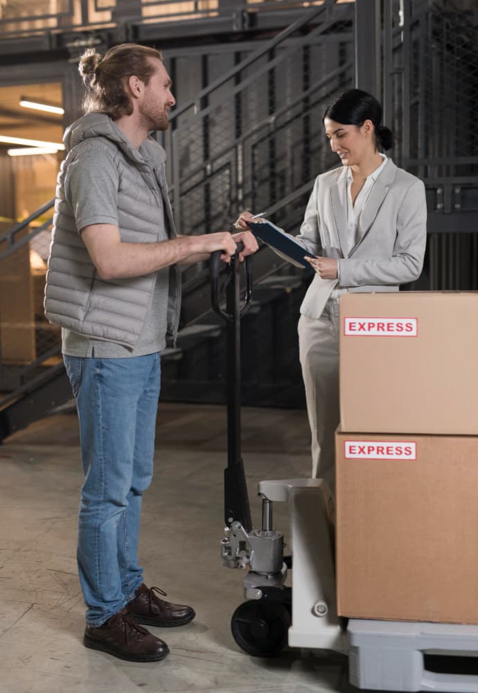 A worker and a receiver checking a handoff beside loaded pallets.